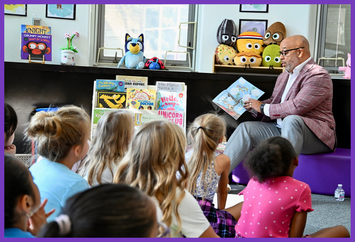 Superintendent Card reading a book to elementary students in a library space